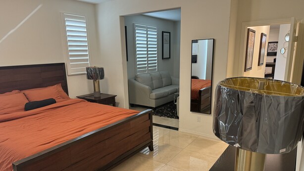 Un dormitorio moderno con una cama de madera, una lámpara de noche, un sofá gris y un espejo grande.