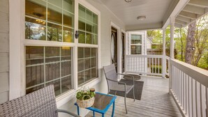 A covered porch with a table and chairs, large windows, and a hanging light fixture.