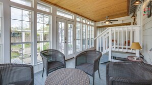 A covered porch with wicker furniture, large windows, and a wooden ceiling.