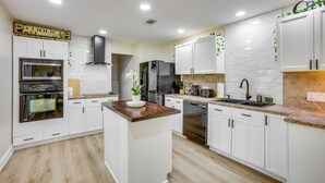 A modern kitchen with white cabinets, a central island, stainless steel appliances, and a marble countertop.