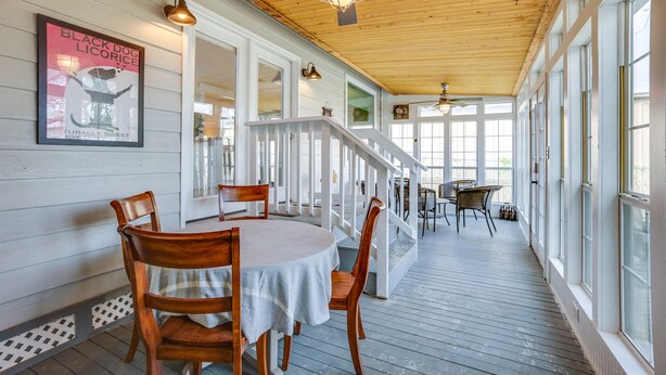 A covered porch with a wooden ceiling, white railings, and a table with chairs.