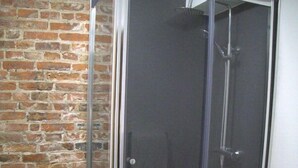 A glass-enclosed shower with a tiled floor and a brick wall. - Old Dutch Embassy by Guestz (Kingston-upon-Hull)