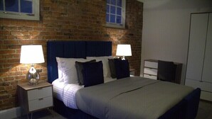 A bedroom with a brick wall, a large bed with a headboard, two bedside tables with lamps, and a wardrobe. - Old Dutch Embassy by Guestz (Kingston-upon-Hull)