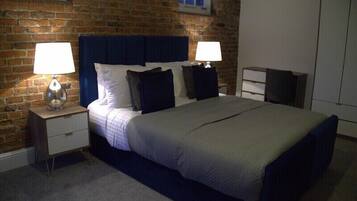A bedroom with a brick wall, a large bed with a headboard, two bedside tables with lamps, and a wardrobe.