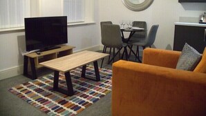 A modern living room with a TV, a small table, a sofa, and a dining area with chairs and a table. - Old Dutch Embassy by Guestz (Kingston-upon-Hull)