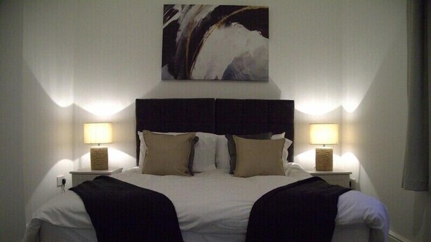 A double bed with a black headboard, two bedside lamps, and a large abstract painting above the bed. - Old Dutch Embassy by Guestz (Kingston-upon-Hull)