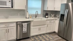 A modern kitchen with white cabinets, stainless steel appliances, a dishwasher, and a window with blinds. - Summer Fun! New Port Richey Fl

 (New Port Richey)