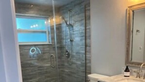 A modern bathroom with a glass-enclosed shower, a white toilet, and a dark vanity with a mirror. - Summer Fun! New Port Richey Fl

 (New Port Richey)