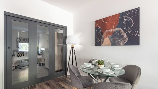 A dining area with a glass table, grey upholstered chairs, a modern lamp, and a contemporary painting. - Binding House by Guestz (Kingston upon Hull)