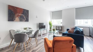 A modern living room with a glass dining table, comfortable seating, a large abstract painting, and a view of the outdoors. - Binding House by Guestz (Kingston upon Hull)
