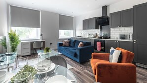 A modern kitchen with dark cabinets, a blue sofa, and an orange armchair. - Binding House by Guestz (Kingston upon Hull)