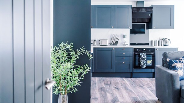 Una cocina moderna con armarios oscuros, horno empotrado y comedor con sofá gris.