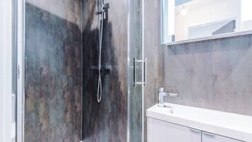 Un baño moderno con ducha envuelta en vidrio, un tocador blanco y un espejo grande.