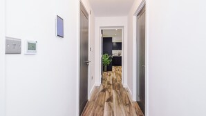 Un pasillo con piso de madera, paredes blancas y una puerta que da a una habitación con un mueble oscuro.