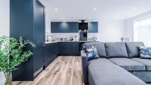 Una cocina moderna con armarios oscuros, horno empotrado y comedor con sofá gris.