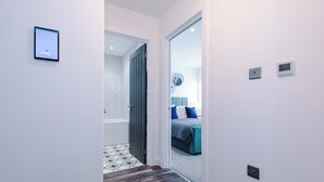 Un corridoio che conduce a una camera da letto con un letto, un comodino e un pannello di controllo a parete.