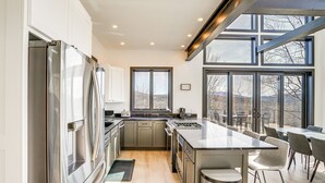 Een moderne keuken met roestvrijstalen apparatuur, een groot eiland en uitzicht op de omgeving door grote ramen.