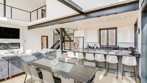 Een moderne keuken met een centraal eiland, een eethoek met een grote tafel en stoelen, en een trap die twee verdiepingen verbindt.