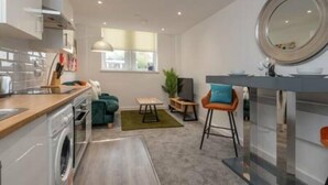 A modern kitchen with a washing machine, a dining area with a table and chairs, a sofa, and a large mirror. - Thornhill House by Guestz (Wakefield)