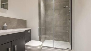 A modern bathroom with a glass shower enclosure, a white toilet, and a dark-colored vanity with a soap dispenser. - Thornhill House by Guestz (Wakefield)