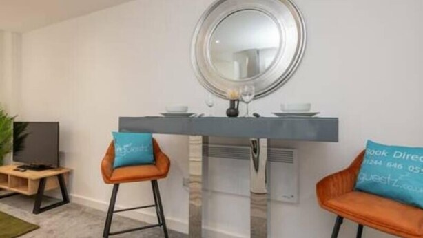 A modern living room with a central table, two bar stools, a television, and a large mirror. - Thornhill House by Guestz (Wakefield)