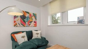 A living room with a green sofa, a wooden coffee table, a colorful abstract painting, and a window with a view of the outside. - Thornhill House by Guestz (Wakefield)