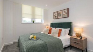 A bedroom with a bed, bedside lamps, a nightstand, a window with blinds, and wall art. - Thornhill House by Guestz (Wakefield)