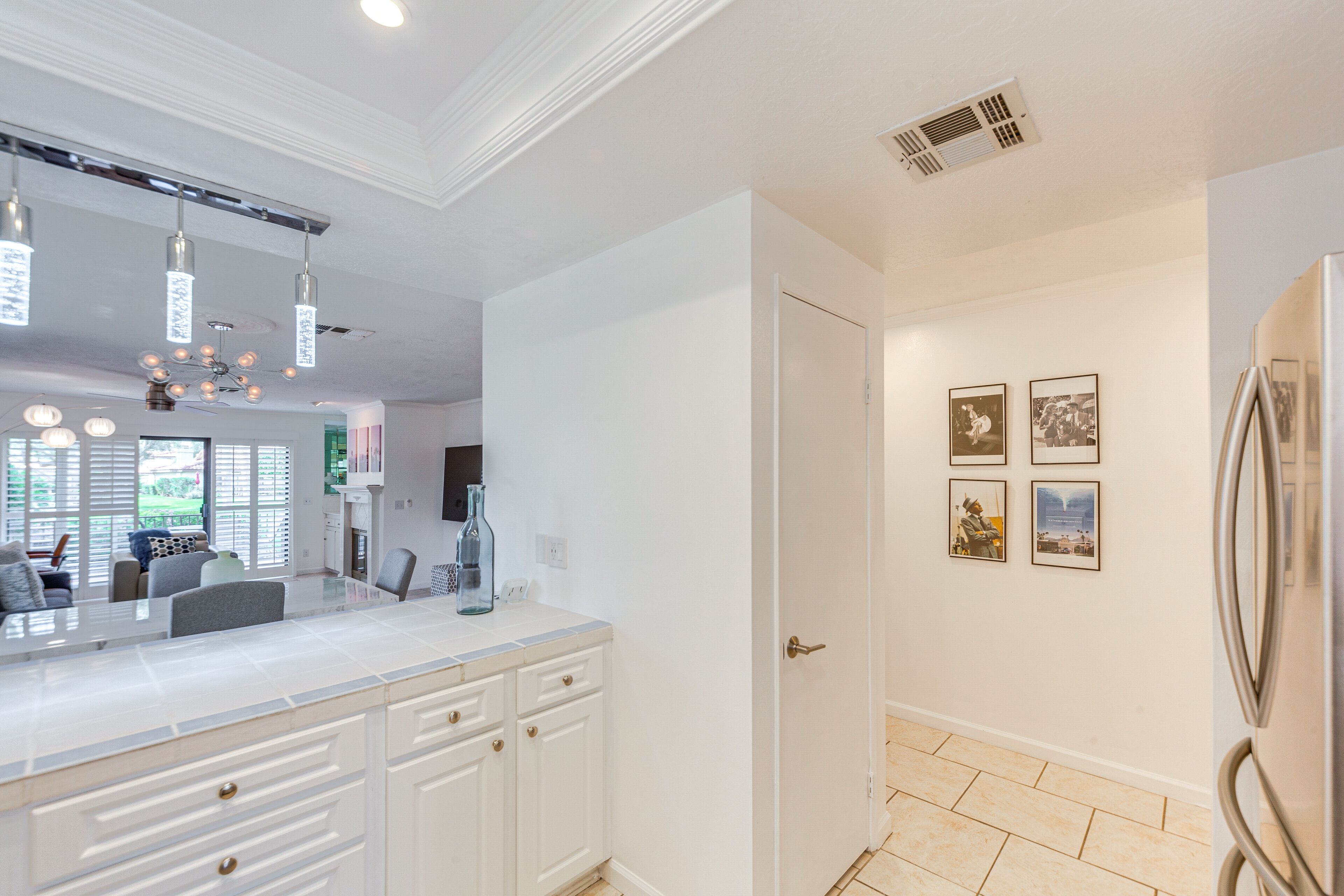 Une cuisine moderne avec des meubles blancs, un grand îlot central, des luminaires suspendus et un réfrigérateur.