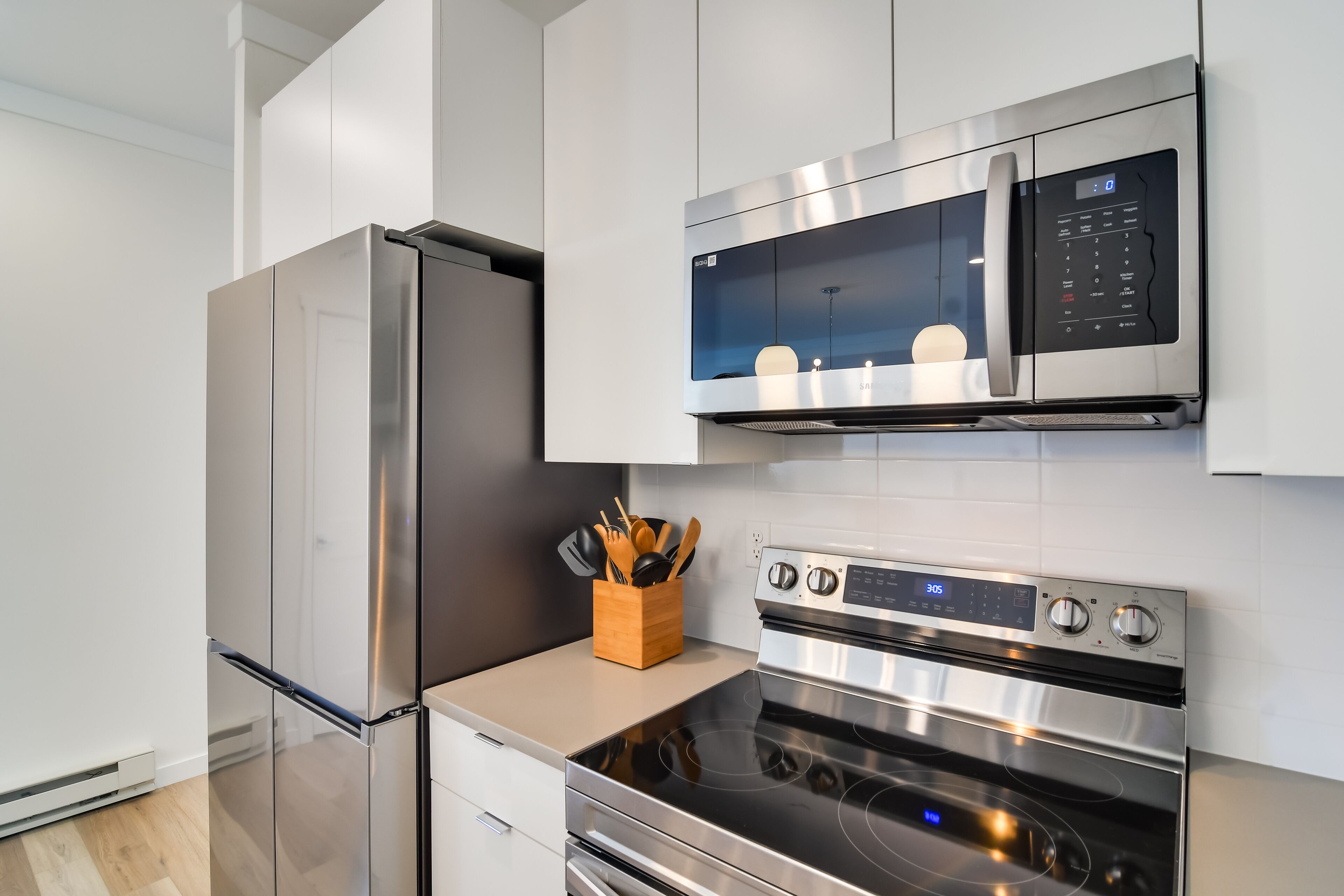 A modern kitchen with stainless steel appliances, including a refrigerator, microwave, and oven, with a wooden utensil holder on the countertop.