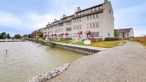 A multi-story hotel with a waterfront view, a covered outdoor seating area, and a gravel pathway along the water's edge. - Lakefront Port Clinton Condo w/ Boat Dock & Slip! (Port Clinton)