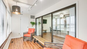 A modern living room with wooden flooring, a glass door leading to a balcony, and orange furniture. - Lakefront Port Clinton Condo w/ Boat Dock & Slip! (Port Clinton)