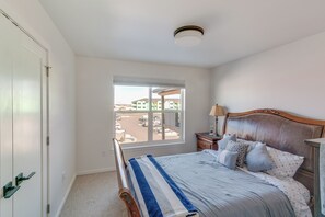 Een slaapkamer met een bed, nachtkastje, lamp, raam met uitzicht op een parkeerplaats en gebouwen, en een deur.