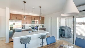 Cozinha moderna com eletrodomésticos de aço inoxidável, uma ilha central com banquetas e uma grande janela com vista para uma área externa coberta.