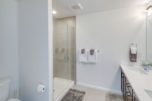 Een moderne badkamer met een douchecabine van glas, witte wanden en een witte wastafel met spiegel.