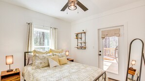 A bedroom with a bed, bedside tables, a ceiling fan, a window with curtains, a door leading to an outdoor deck, and a wall-mounted shelf with plants. - Winnsboro Barndominium w/ Fire Pit & Large Deck! (Winnsboro)