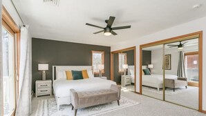 A bedroom with a large bed, bedside tables, a bench, a ceiling fan, and a sliding glass door leading to another room. - Lakeview w/Pool, Hot Tub, Firepit, Gameroom, Golf! (Penn Yan)