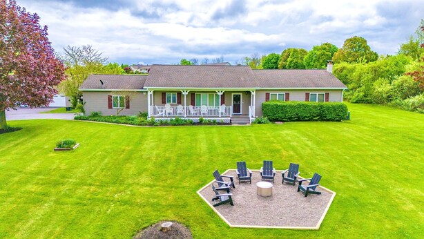 A two-story house with a porch, a lawn, and a fire pit area with chairs. - Lakeview w/Pool, Hot Tub, Firepit, Gameroom, Golf! (Penn Yan)