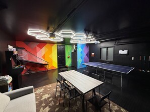 Ein Raum mit einer Tischtennisplatte, Stühlen, einem kleinen Basketballkorb und einem farbenfrohen Wanddesign.