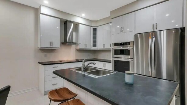 A modern kitchen with stainless steel appliances, white cabinetry, and a black countertop. - Detached 4 Bedroom (Brant)