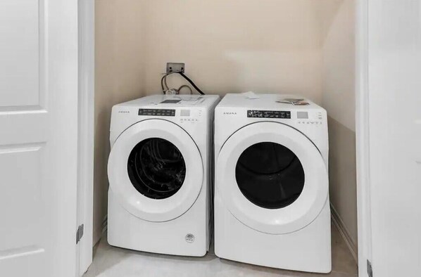 Deux machines à laver à chargement frontal, de couleur blanche, dans une petite buanderie avec un mur beige et une porte blanche.
