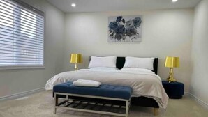 A bedroom with a bed, two bedside lamps, a bench, and a painting on the wall.