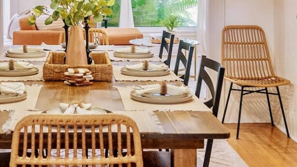 Un comedor con una mesa larga dispuesta para seis personas, rodeada de sillas de mimbre.