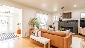 Una sala de estar con sofá, banca, chimenea y puerta que da a otra habitación.