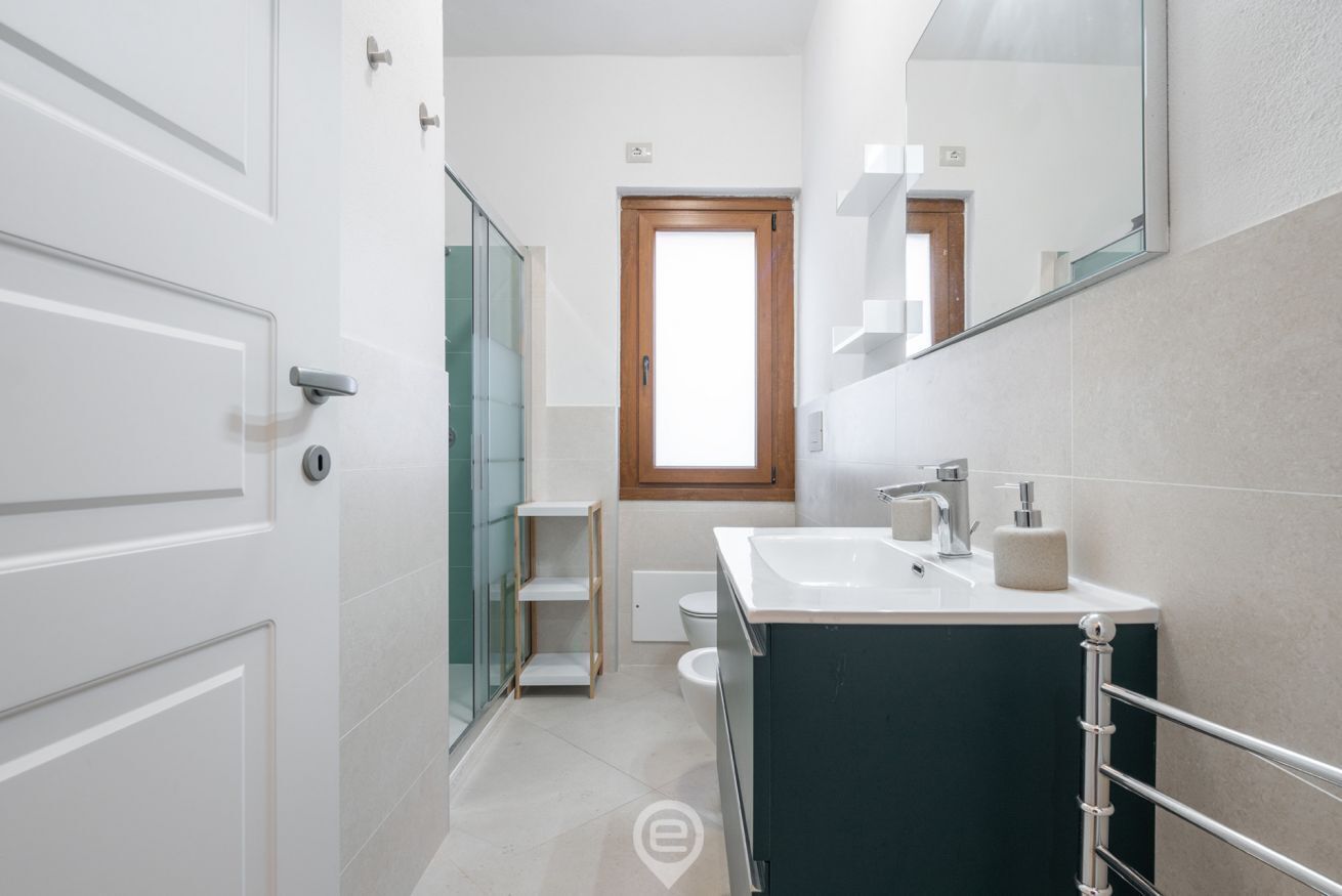 A modern bathroom with a dark vanity, a glass shower enclosure, and a window providing natural light.