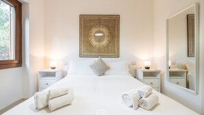 A hotel room with a large bed, two bedside tables, a wall-mounted artwork, a mirror, and a window.