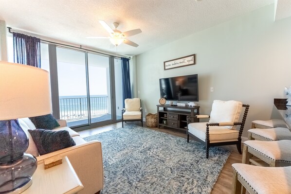 A living room with a sofa, chairs, a TV, and a large window with curtains.