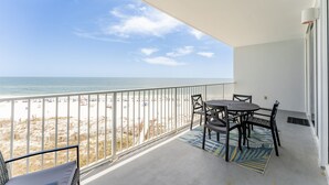 A balcony with a view of the beach, a table with chairs, and a patterned rug. - Lighthouse w/ Bunk Room.  3 Pools!  Beachfront-  Free Daily Activities (Gulf Shores)