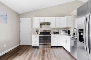 Una cocina moderna con armarios blancos, un refrigerador de acero inoxidable, un microondas, una estufa y un lavavajillas.