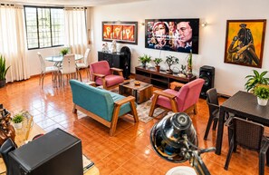 Una sala de estar con sofá, sillas, una mesa de centro, televisor y un cuadro en la pared.