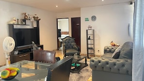 Una sala de estar con televisor, sofás de cuero, una mesa de centro de vidrio y un ventilador.